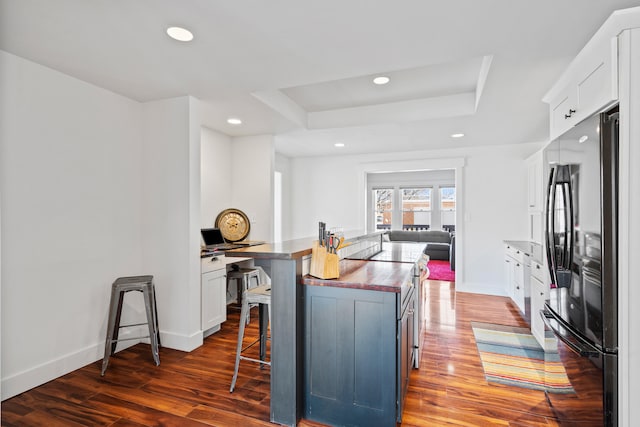 kitchen featuring wood finished floors, white cabinetry, a tray ceiling, freestanding refrigerator, and a kitchen bar