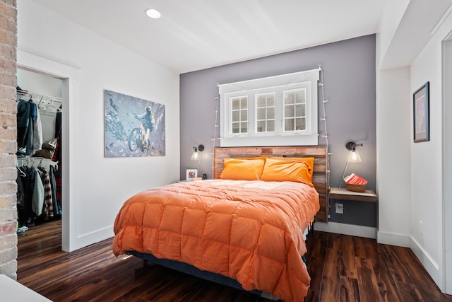 bedroom featuring a walk in closet, wood finished floors, baseboards, and a closet