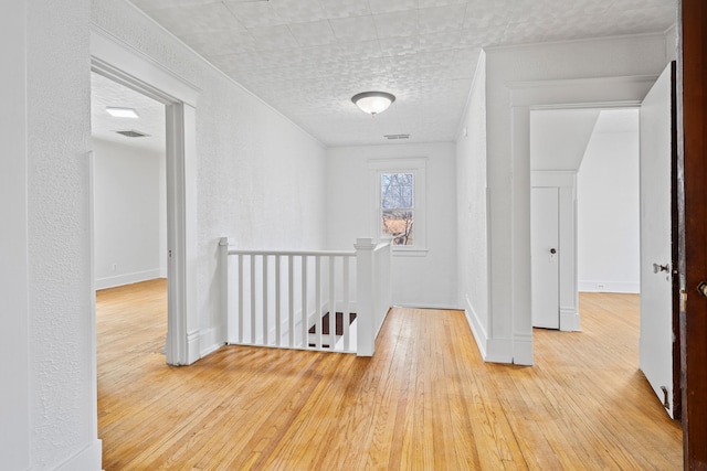 hall with visible vents, an upstairs landing, hardwood / wood-style flooring, baseboards, and a textured wall