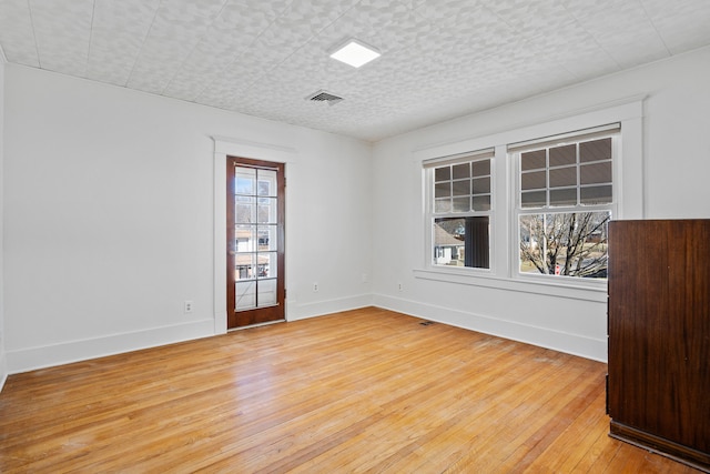 empty room featuring light wood-style flooring, baseboards, visible vents, and a textured ceiling