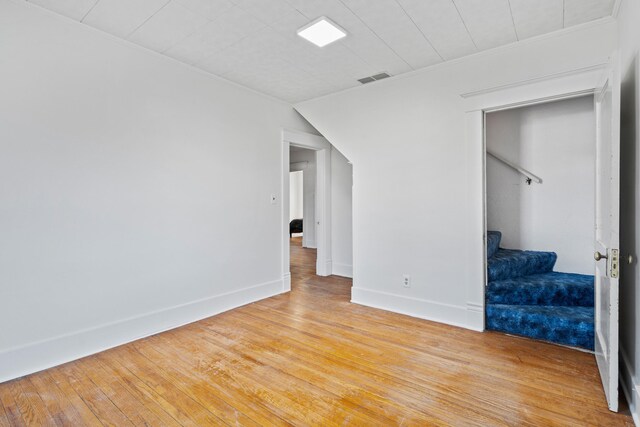 empty room with visible vents, stairs, light wood-type flooring, and baseboards