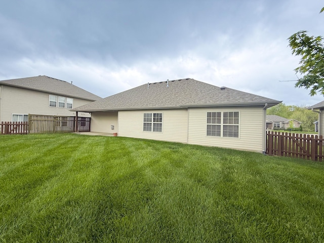 back of house featuring a lawn, a shingled roof, and a fenced backyard