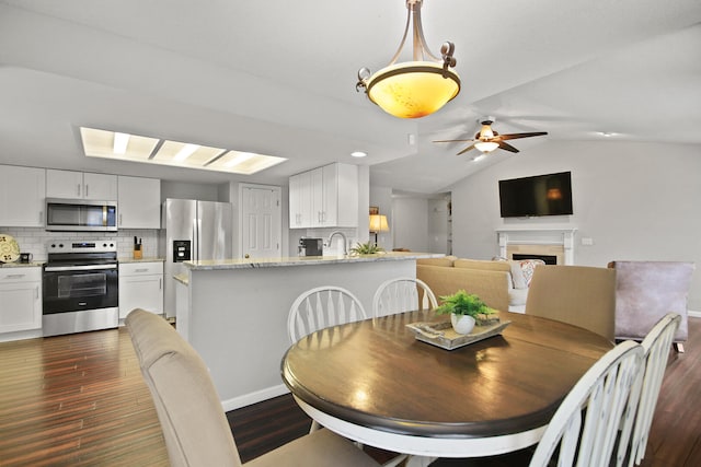 dining space with ceiling fan, a fireplace, dark wood-type flooring, and lofted ceiling