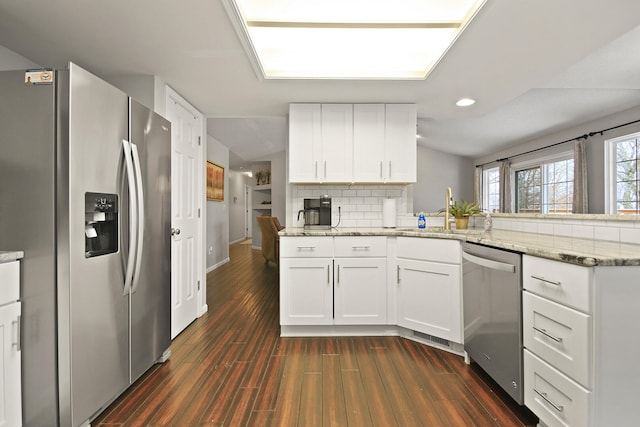 kitchen featuring a sink, tasteful backsplash, stainless steel appliances, a peninsula, and dark wood-style flooring