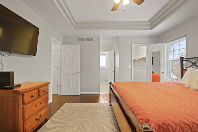 bedroom featuring visible vents, ceiling fan, baseboards, a tray ceiling, and dark wood-style flooring