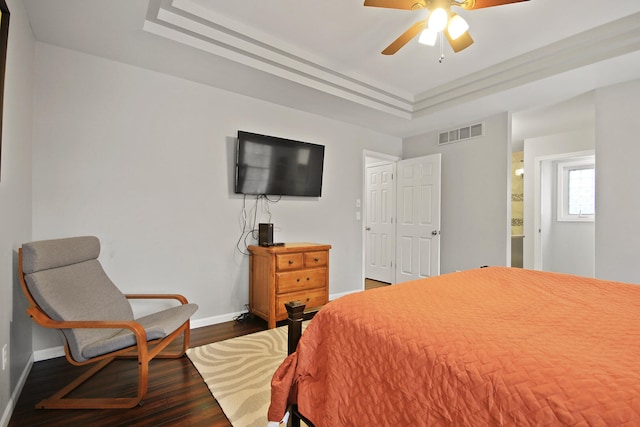 bedroom with visible vents, baseboards, a tray ceiling, and wood finished floors