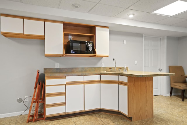 kitchen featuring a sink, a peninsula, white cabinets, and black microwave