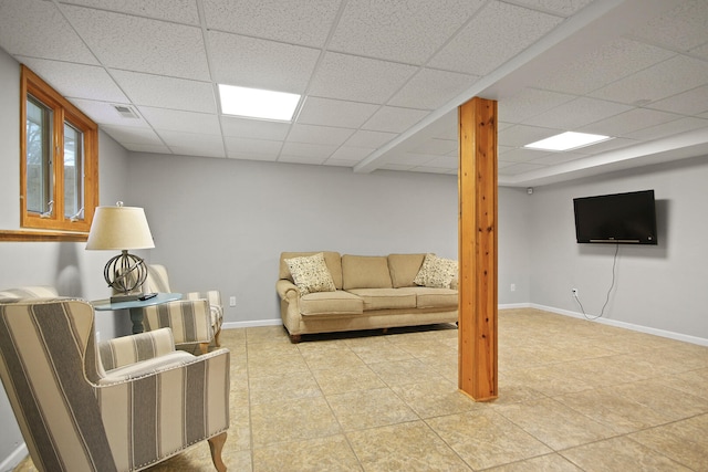 living room featuring a drop ceiling, baseboards, and light tile patterned flooring