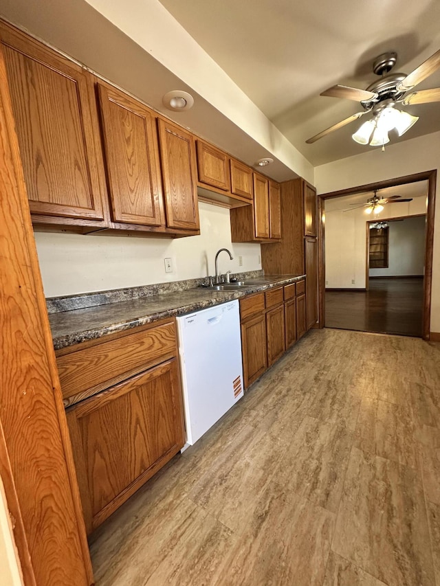 kitchen featuring dark countertops, light wood finished floors, brown cabinets, white dishwasher, and a sink