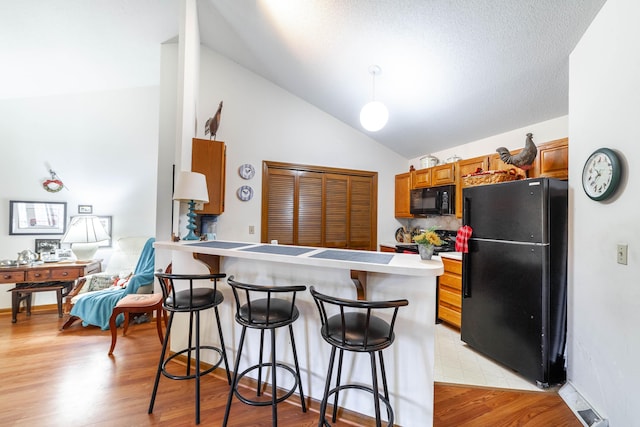 kitchen featuring a peninsula, black appliances, light wood-style floors, a kitchen bar, and brown cabinets