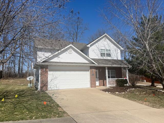 view of front of property featuring a front yard, a porch, concrete driveway, a garage, and brick siding