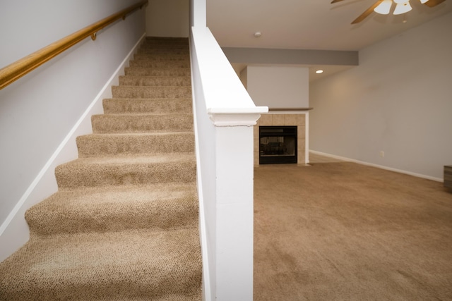 stairs with baseboards, carpet floors, a ceiling fan, and a tile fireplace