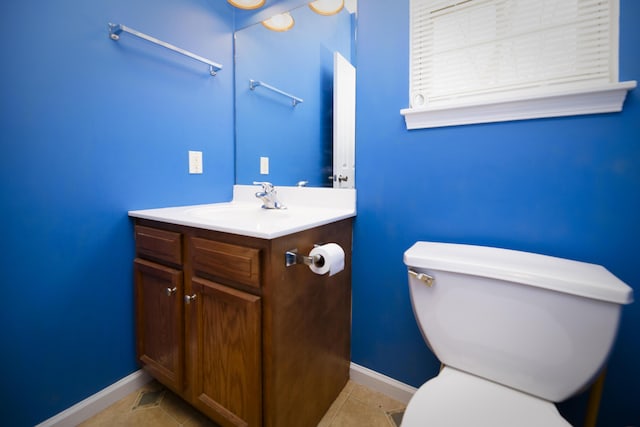 half bath featuring tile patterned flooring, toilet, vanity, and baseboards