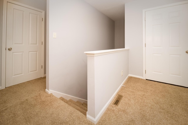 hallway featuring carpet, an upstairs landing, visible vents, and baseboards