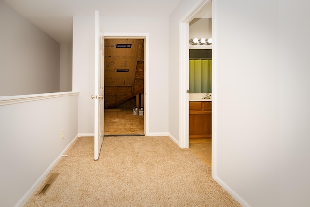 hallway with light carpet, visible vents, and baseboards