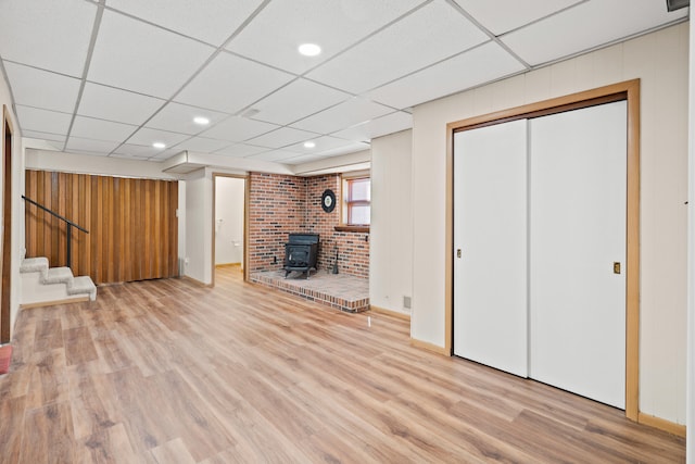 basement featuring stairway, a wood stove, light wood-type flooring, and a drop ceiling