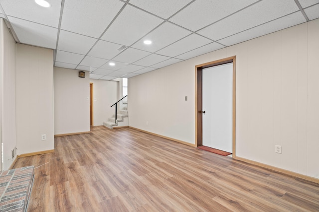 finished below grade area featuring baseboards, stairs, light wood-type flooring, and a paneled ceiling