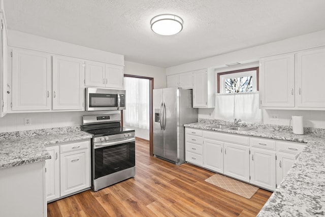 kitchen featuring light wood-style flooring, a sink, light stone counters, white cabinetry, and appliances with stainless steel finishes