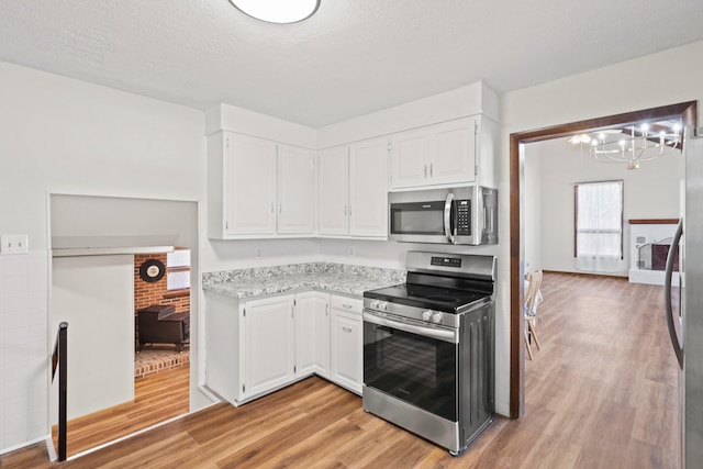 kitchen featuring white cabinetry, stainless steel appliances, light wood finished floors, light stone countertops, and a chandelier