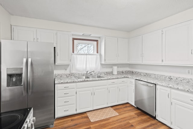 kitchen featuring white cabinets, wood finished floors, appliances with stainless steel finishes, and a sink