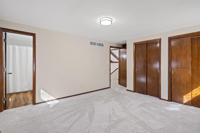 unfurnished bedroom featuring visible vents, two closets, a textured ceiling, carpet flooring, and baseboards