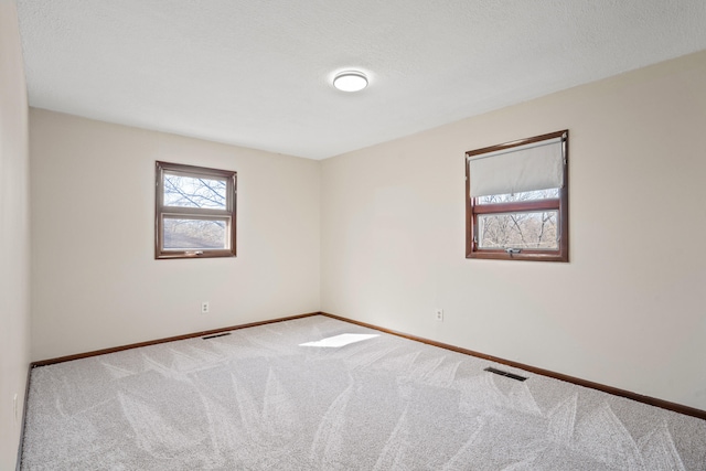 empty room with carpet flooring, visible vents, a textured ceiling, and baseboards