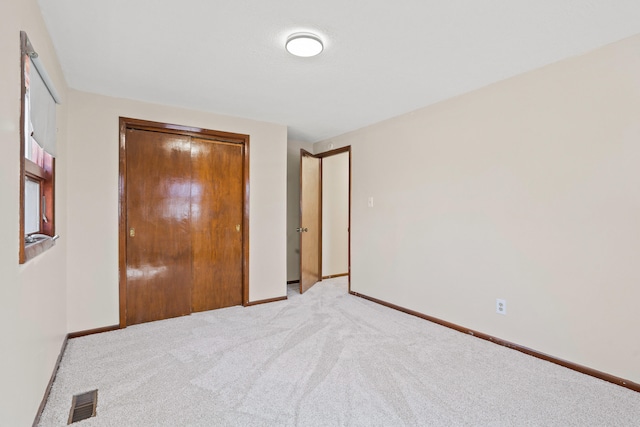 unfurnished bedroom featuring a closet, light carpet, baseboards, and visible vents