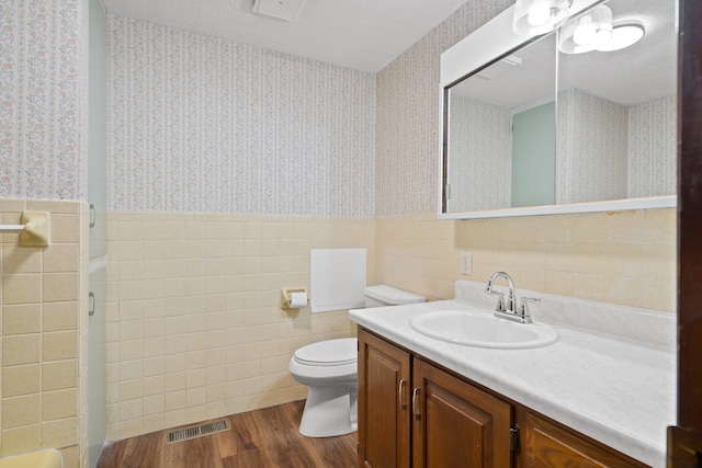 full bath featuring a wainscoted wall, visible vents, wood finished floors, and wallpapered walls