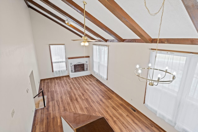 unfurnished living room with visible vents, a fireplace with raised hearth, vaulted ceiling with beams, ceiling fan with notable chandelier, and wood finished floors