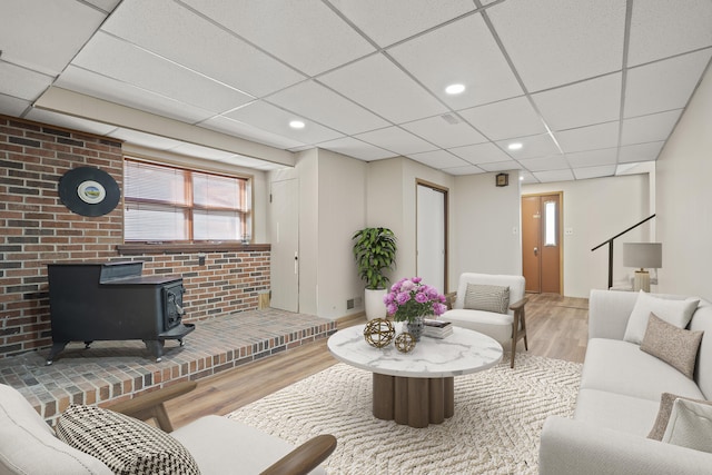 living area with visible vents, a drop ceiling, wood finished floors, recessed lighting, and a wood stove