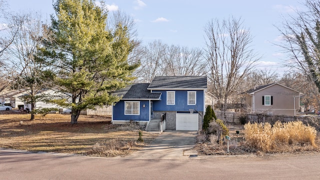 split level home with brick siding, an attached garage, driveway, and fence