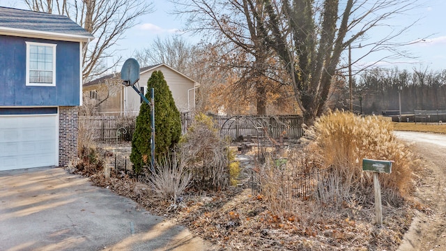 view of home's exterior featuring concrete driveway, a garage, fence, and brick siding