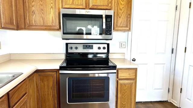 kitchen featuring light countertops, brown cabinets, dark wood-style floors, stainless steel appliances, and a sink