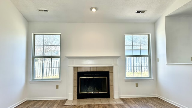 unfurnished living room with wood finished floors, a fireplace, visible vents, and a textured ceiling