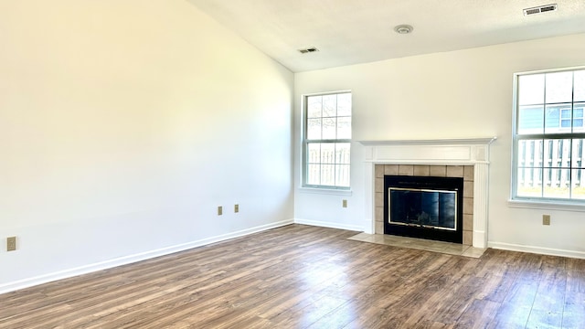 unfurnished living room featuring visible vents, a healthy amount of sunlight, wood finished floors, and a tile fireplace