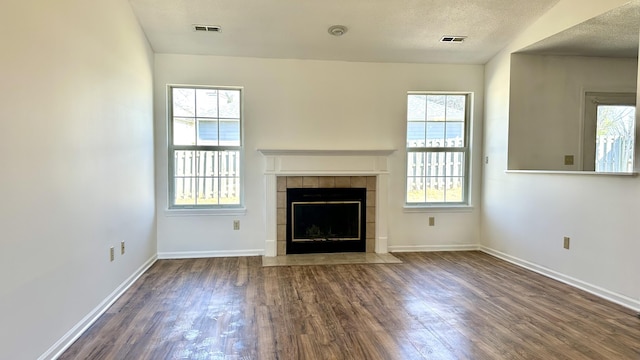 unfurnished living room with a tiled fireplace, wood finished floors, a wealth of natural light, and a textured ceiling