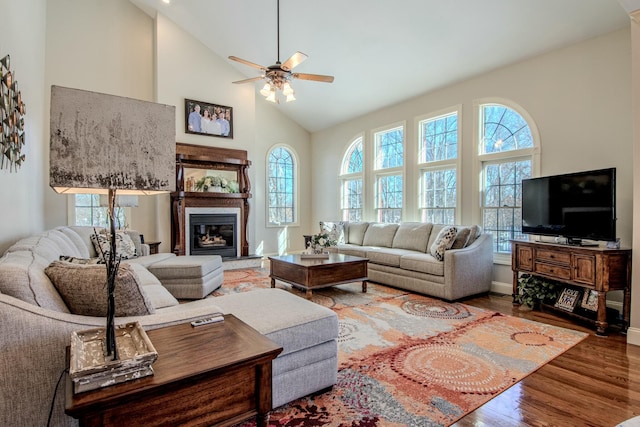 living area featuring a glass covered fireplace, wood finished floors, high vaulted ceiling, and ceiling fan