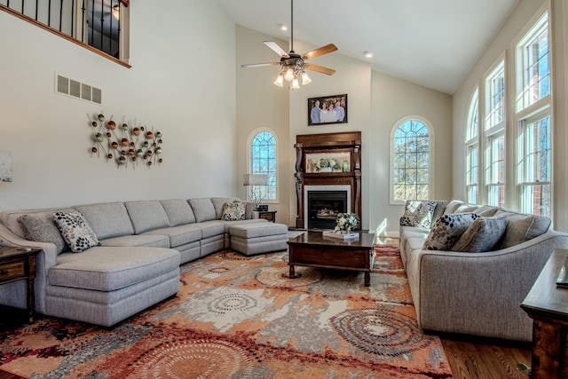 living area with visible vents, high vaulted ceiling, wood finished floors, a fireplace, and ceiling fan