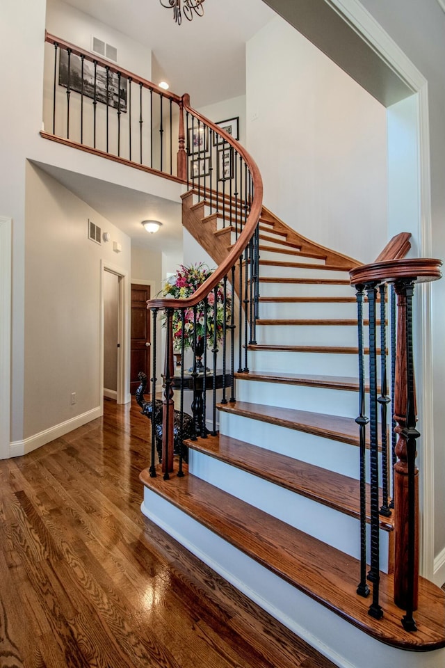 stairway with wood finished floors, visible vents, a towering ceiling, and baseboards