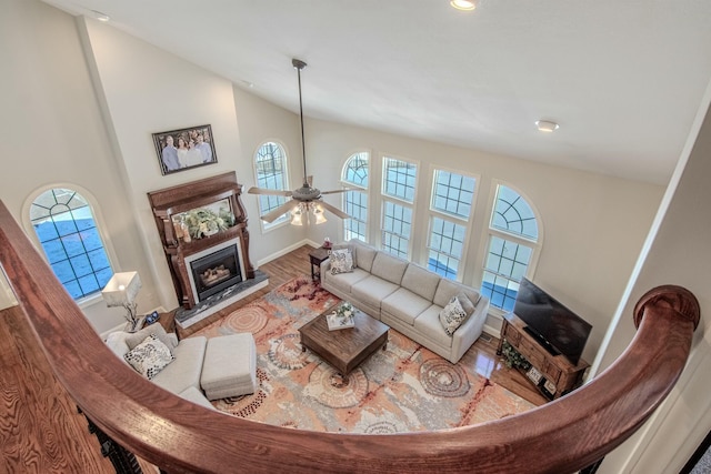 living area with wood finished floors, a fireplace, baseboards, ceiling fan, and vaulted ceiling