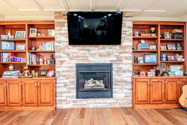 living room with a stone fireplace, light wood-style flooring, and crown molding