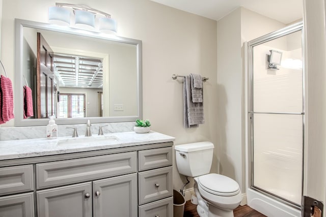 bathroom featuring toilet, a stall shower, wood finished floors, baseboards, and vanity