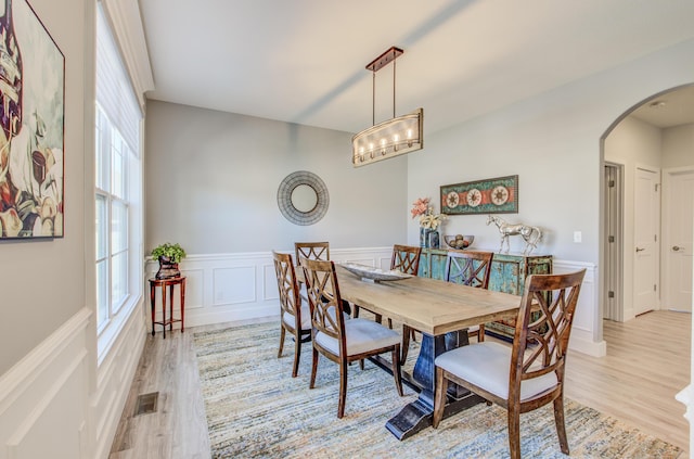 dining area featuring a wainscoted wall, visible vents, arched walkways, and light wood finished floors