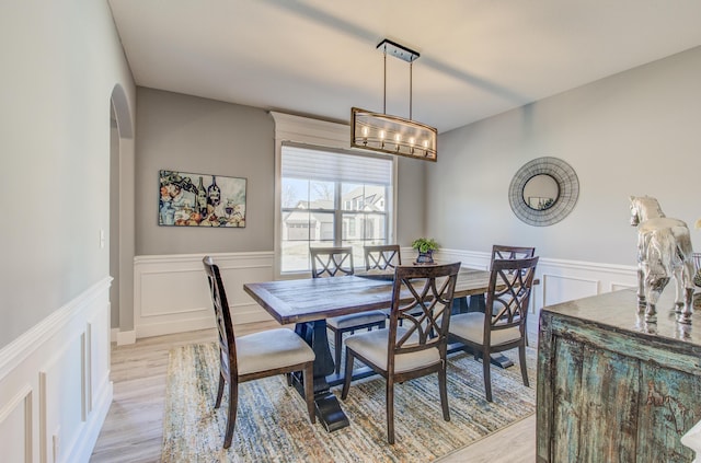 dining space with arched walkways, wainscoting, light wood-style flooring, and an inviting chandelier