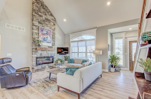 living room with wood finished floors, baseboards, visible vents, high vaulted ceiling, and a stone fireplace