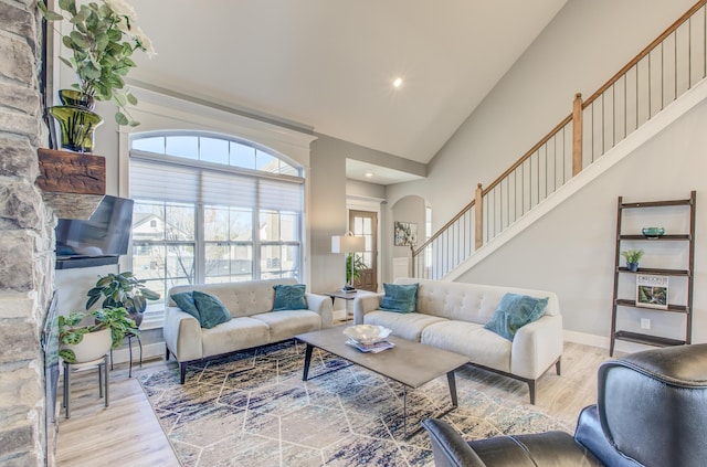 living room featuring stairway, wood finished floors, arched walkways, and high vaulted ceiling