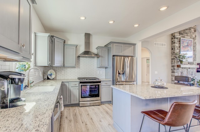 kitchen featuring visible vents, gray cabinetry, a sink, stainless steel appliances, and wall chimney exhaust hood