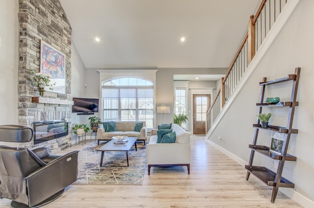 living area with a stone fireplace, stairway, wood finished floors, and baseboards