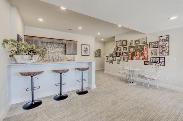 kitchen featuring visible vents, recessed lighting, a peninsula, a breakfast bar area, and light stone countertops