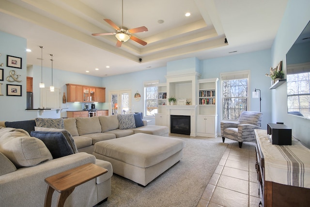 living area featuring ceiling fan, recessed lighting, light tile patterned flooring, a glass covered fireplace, and a raised ceiling